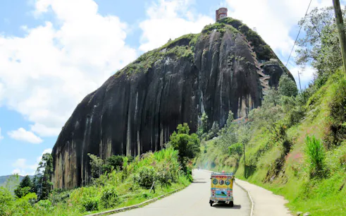 Chiva bus approaching La Piedra de Guatapé rock formation in Colombia.