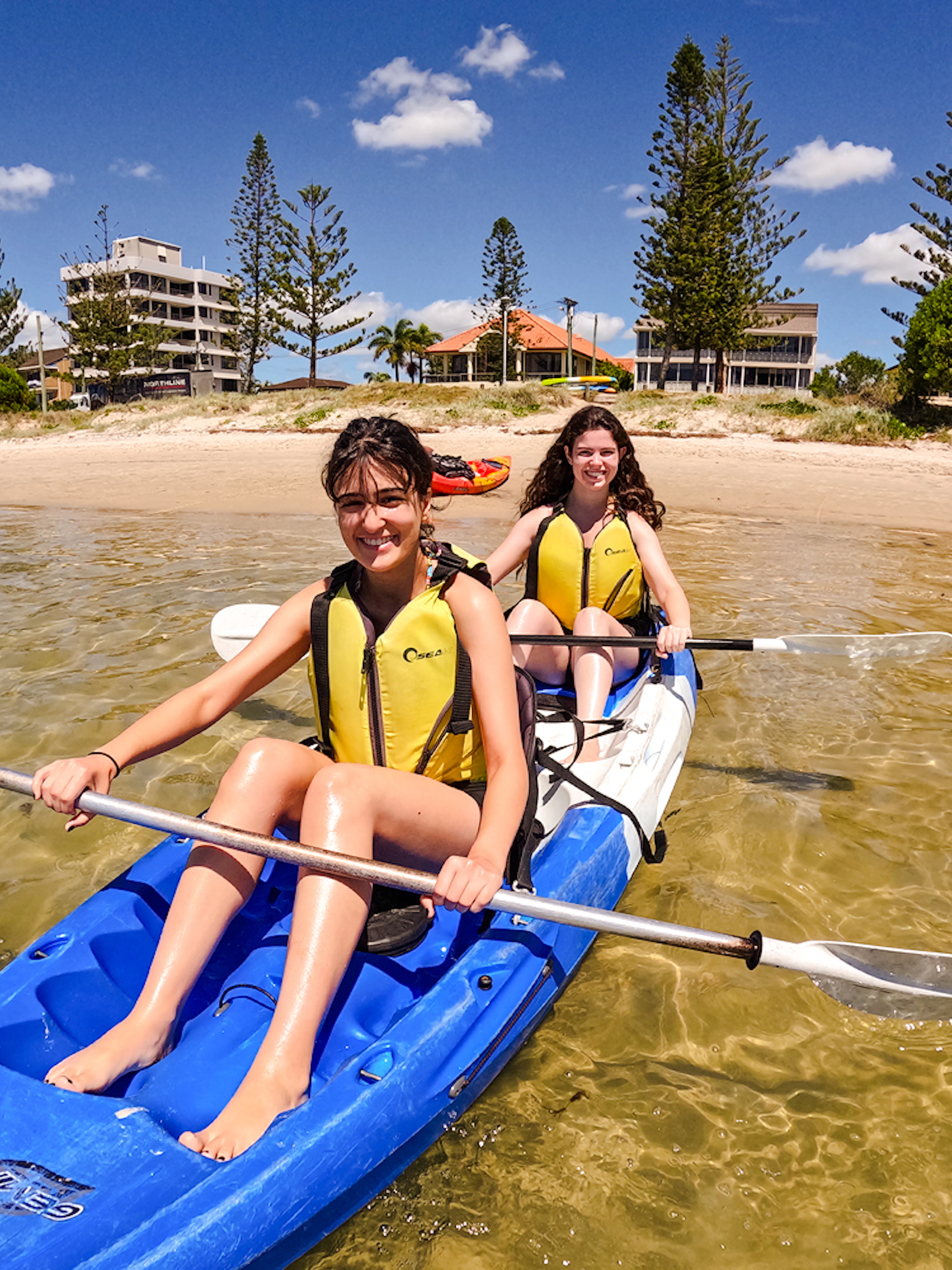Kayakers paddling in Broadwater, Gold Coast with shoreline and buildings in the background.