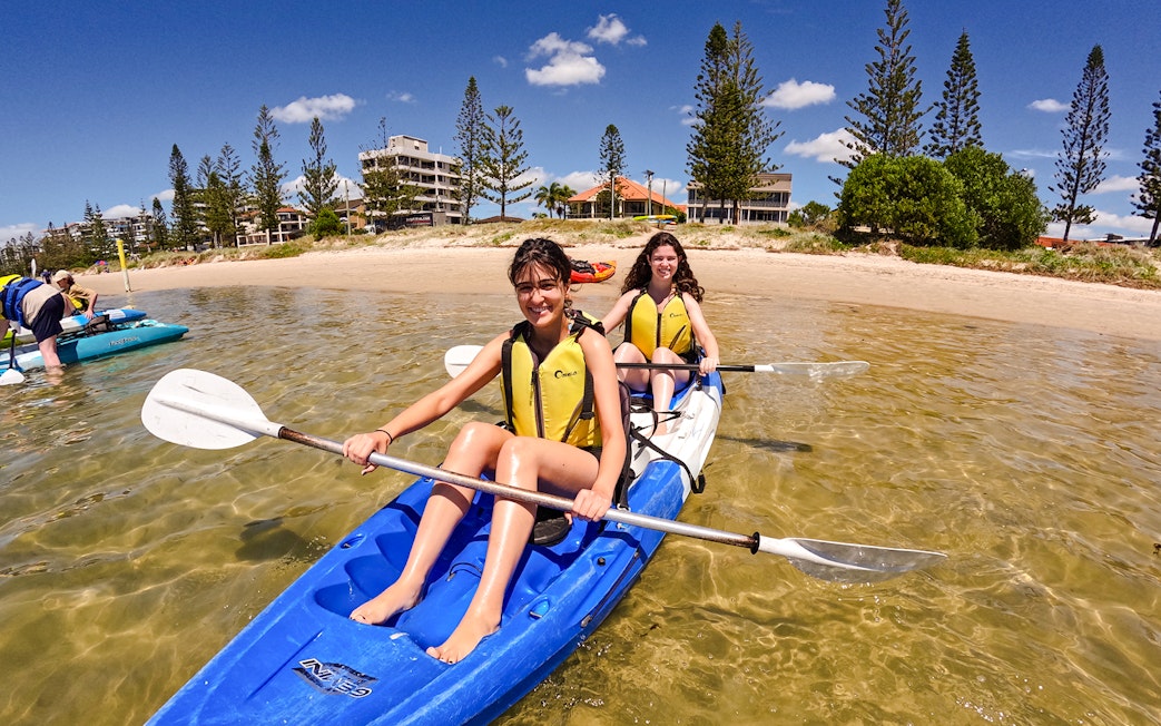 Kayakers paddling in Broadwater, Gold Coast with shoreline and buildings in the background.