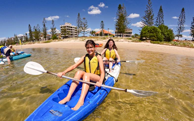 Kayakers paddling in Broadwater, Gold Coast with shoreline and buildings in the background.