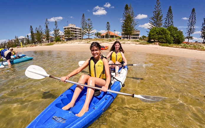 Kayakers paddling in Broadwater, Gold Coast with shoreline and buildings in the background.