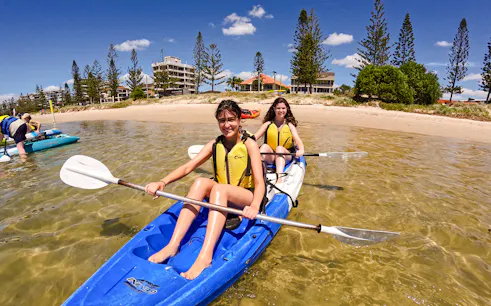 Kayakers paddling in Broadwater, Gold Coast with shoreline and buildings in the background.