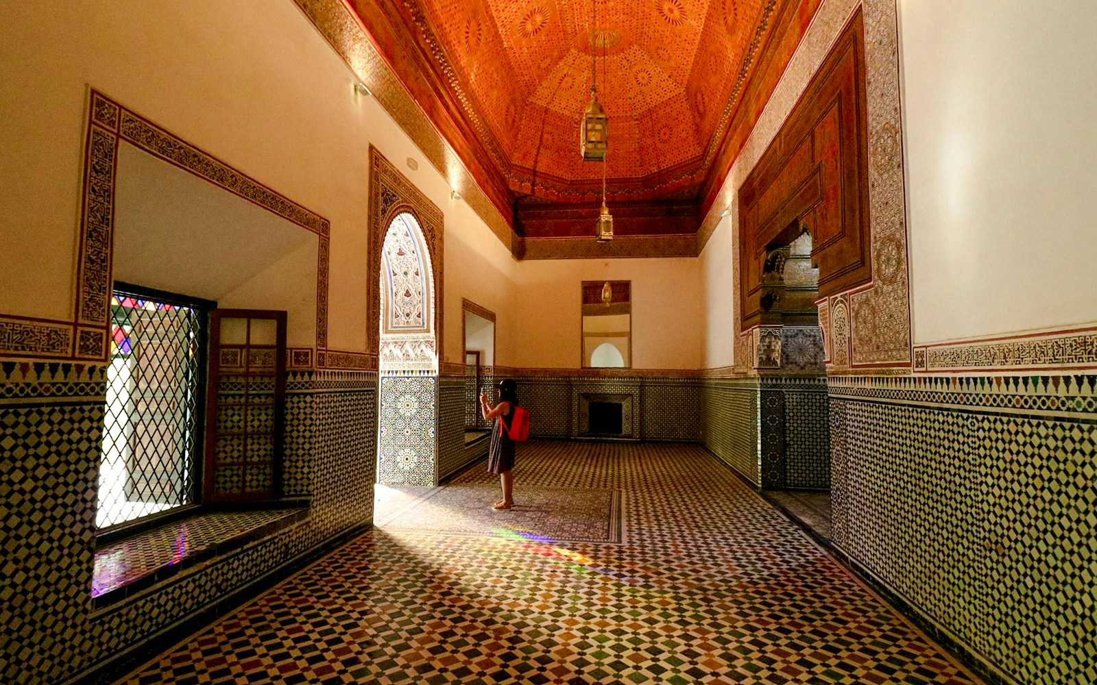 Girl photographing intricate tilework in Bahia Palace hallway, Marrakech.