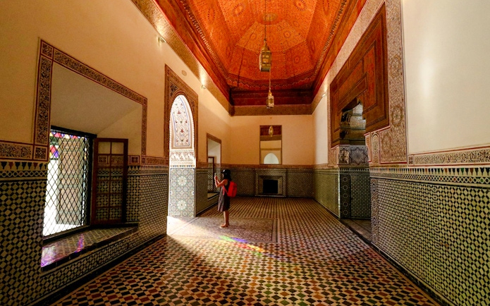 Girl photographing intricate tilework in Bahia Palace hallway, Marrakech.