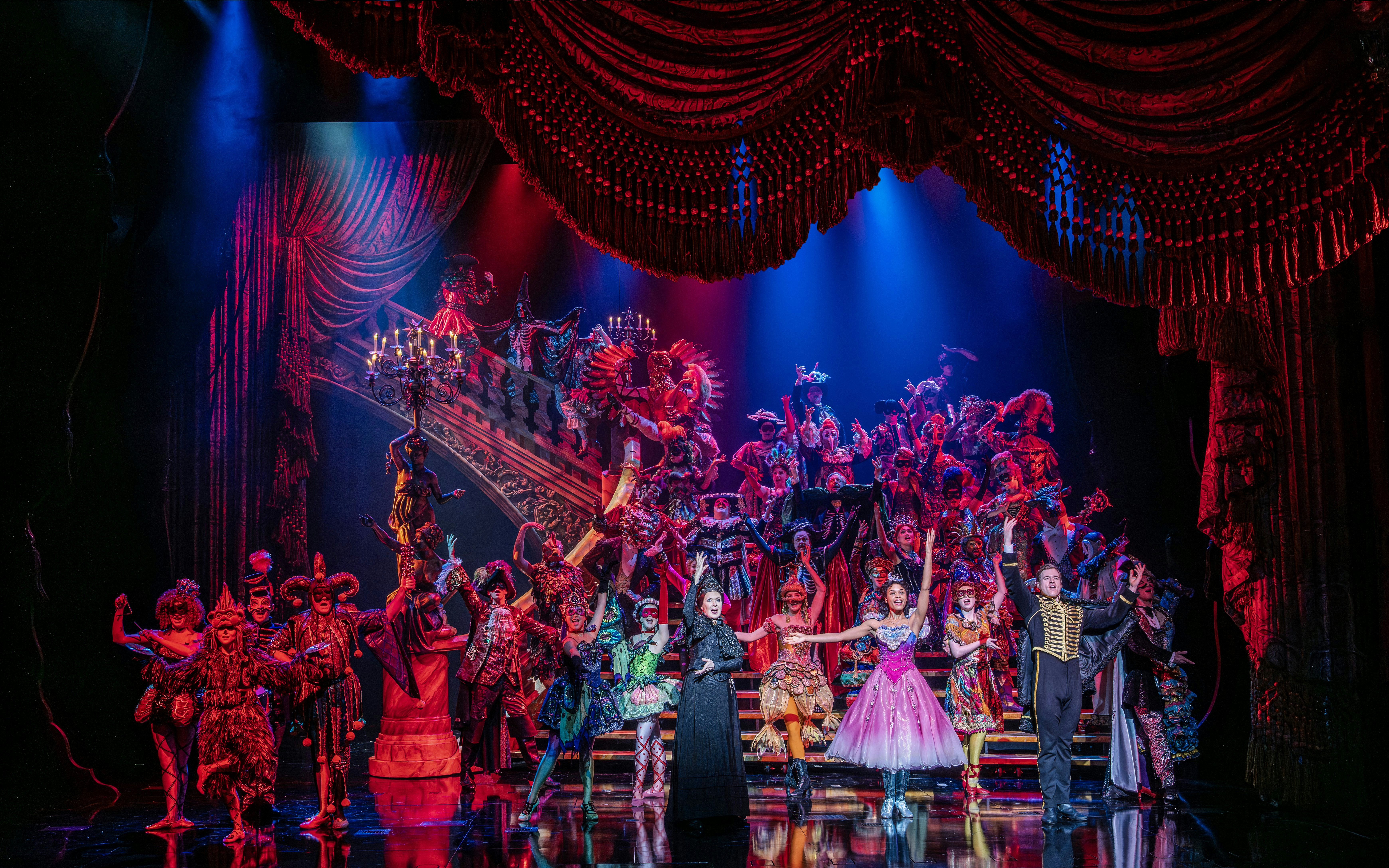 Phantom of the Opera cast performing a vibrant masquerade ball scene on stage.