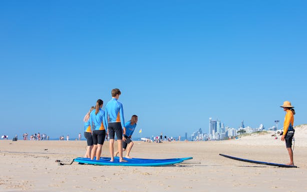 Surf instructor teaching beginners on Gold Coast beach with city skyline in background.