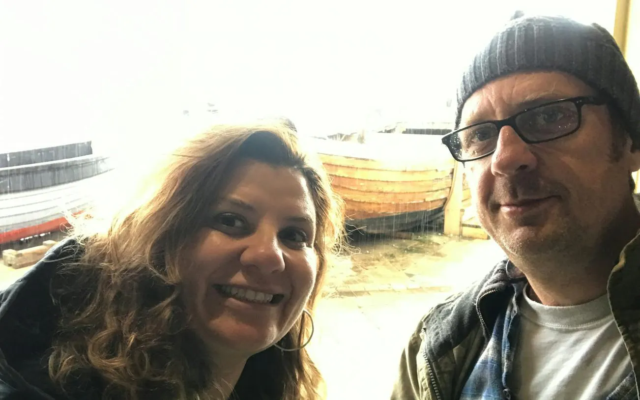 Two people smiling with a wooden boat in the background, Brighton city exploration game.