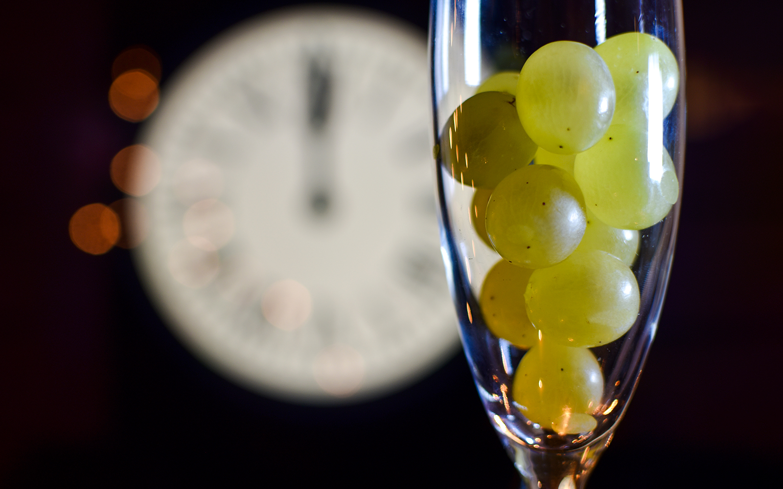 Twelve grapes in a glass with a clock striking midnight, New Year tradition.