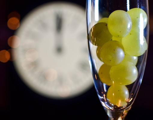 Twelve grapes in a glass with a clock striking midnight, New Year tradition.