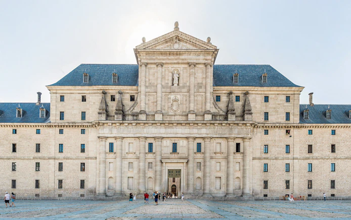 El Escorial courtyard with visitors in front of the historic facade, Spain.