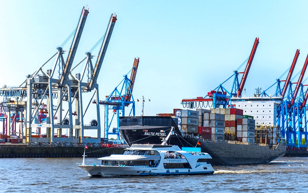 Harbor cruise boat passing container ship and cranes in Hamburg port.