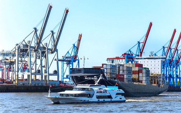 Harbor cruise boat passing container ship and cranes in Hamburg port.