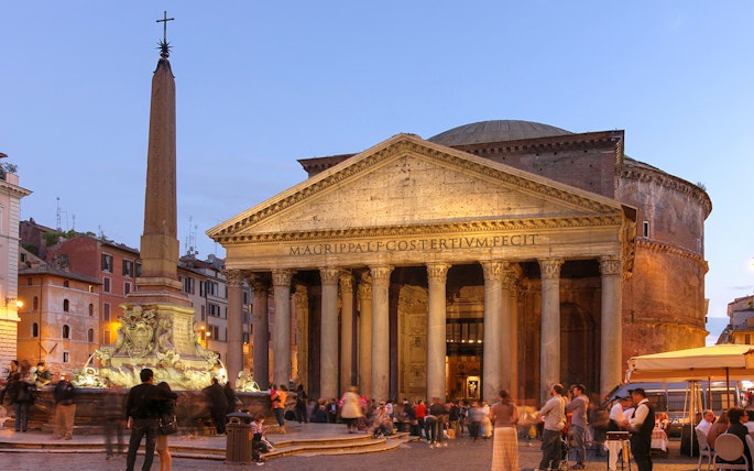 Pantheon in Rome illuminated at dusk with people gathered in the square.