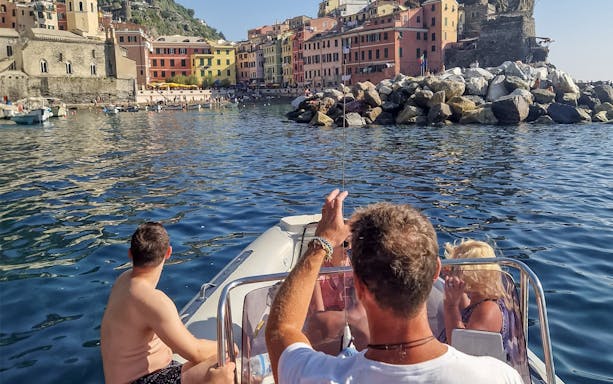 Boat tour in Cinque Terre with view of colorful Vernazza buildings and rocky shoreline.