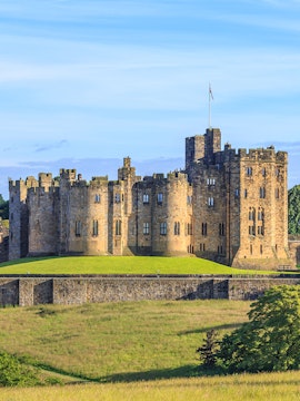Alnwick Castle in Northumberland, England, with lush green grounds.