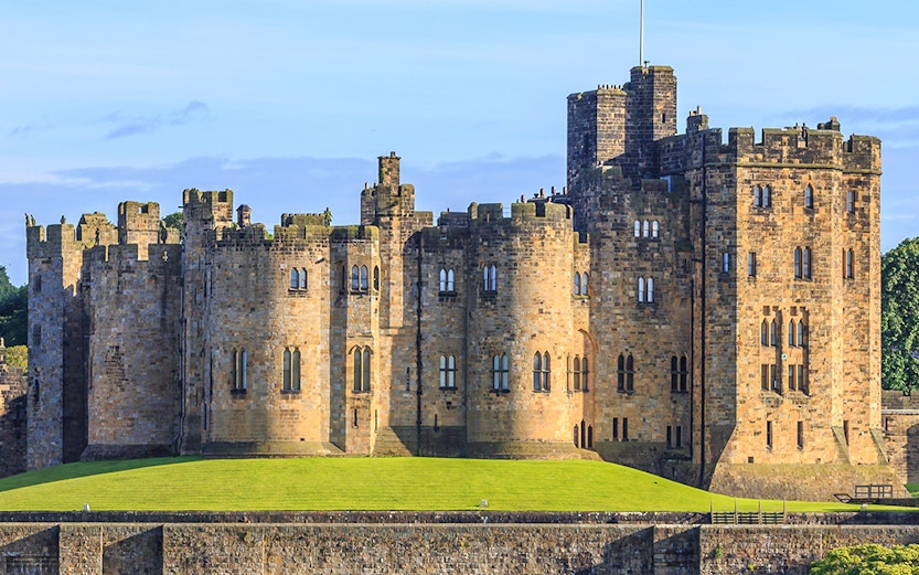 Alnwick Castle in Northumberland, England, with lush green grounds.