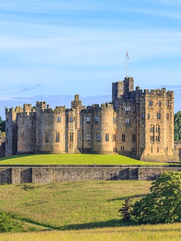 Alnwick Castle in Northumberland, England, with lush green grounds.