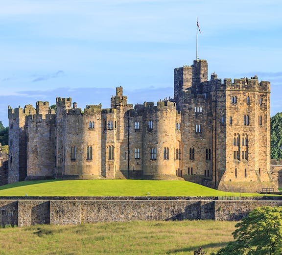 Alnwick Castle in Northumberland, England, with lush green grounds.