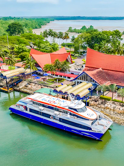Ferry docked at Bintan Resorts terminal with red-roofed buildings and lush greenery.