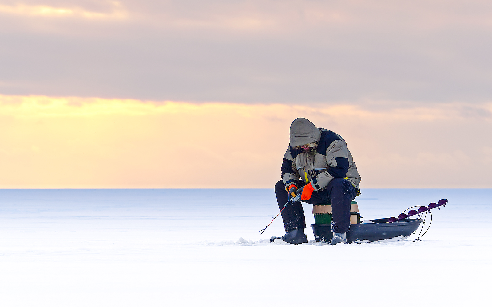 Man ice fishing on a frozen lake in Lapland at sunset.