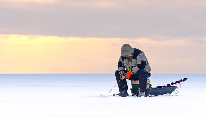 Man ice fishing on a frozen lake in Lapland at sunset.