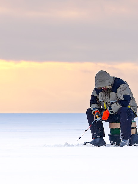 Man ice fishing on a frozen lake in Lapland at sunset.