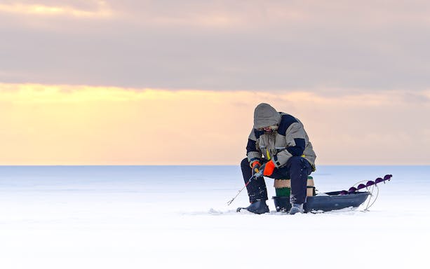 Man ice fishing on a frozen lake in Lapland at sunset.