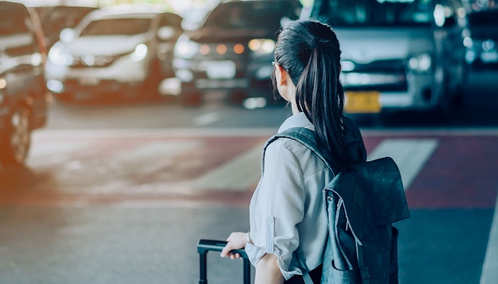 Woman with suitcase waiting for transfer, taxis in background.