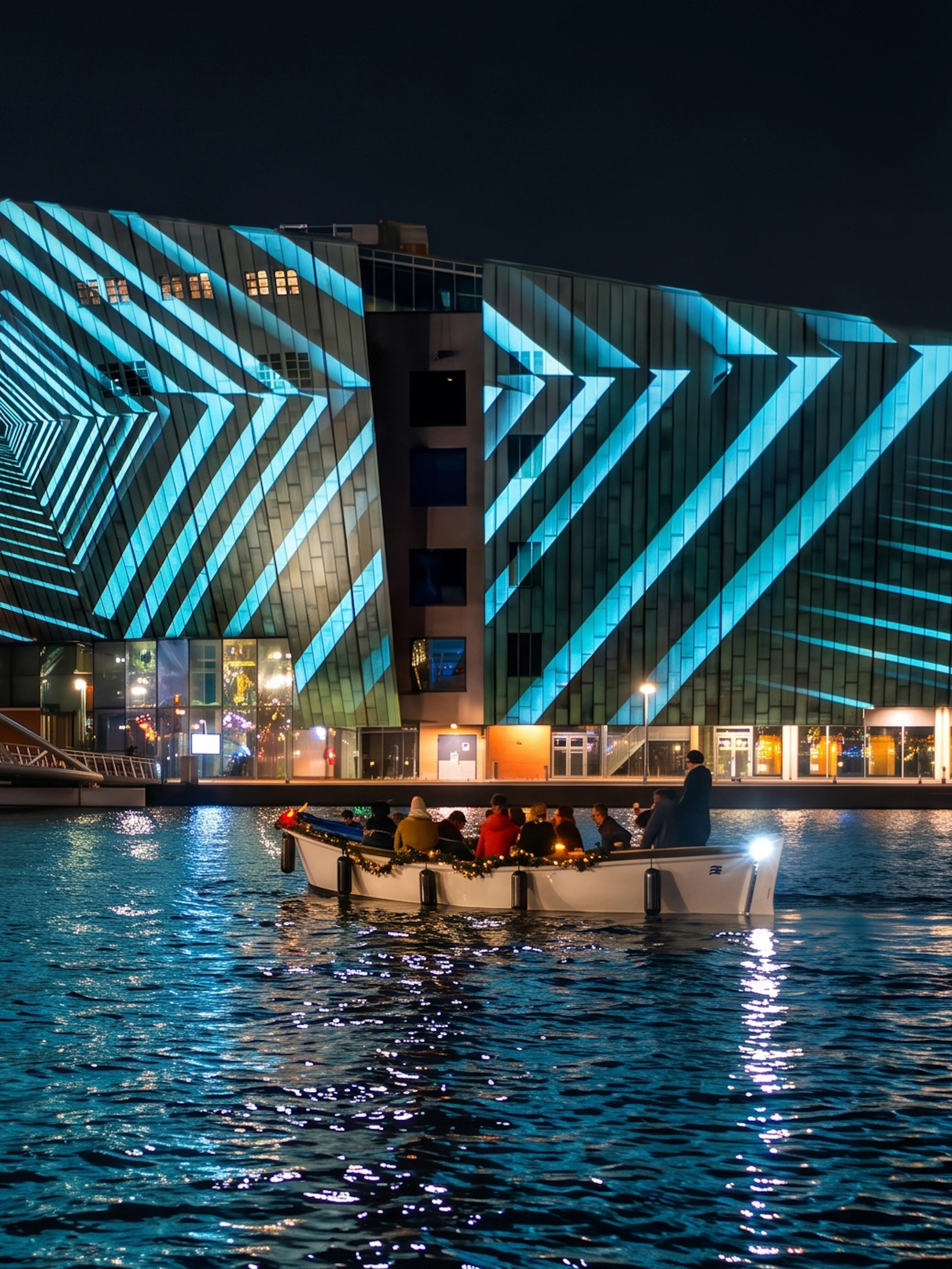 Boat tour at Amsterdam Light Festival with illuminated geometric patterns on a building.