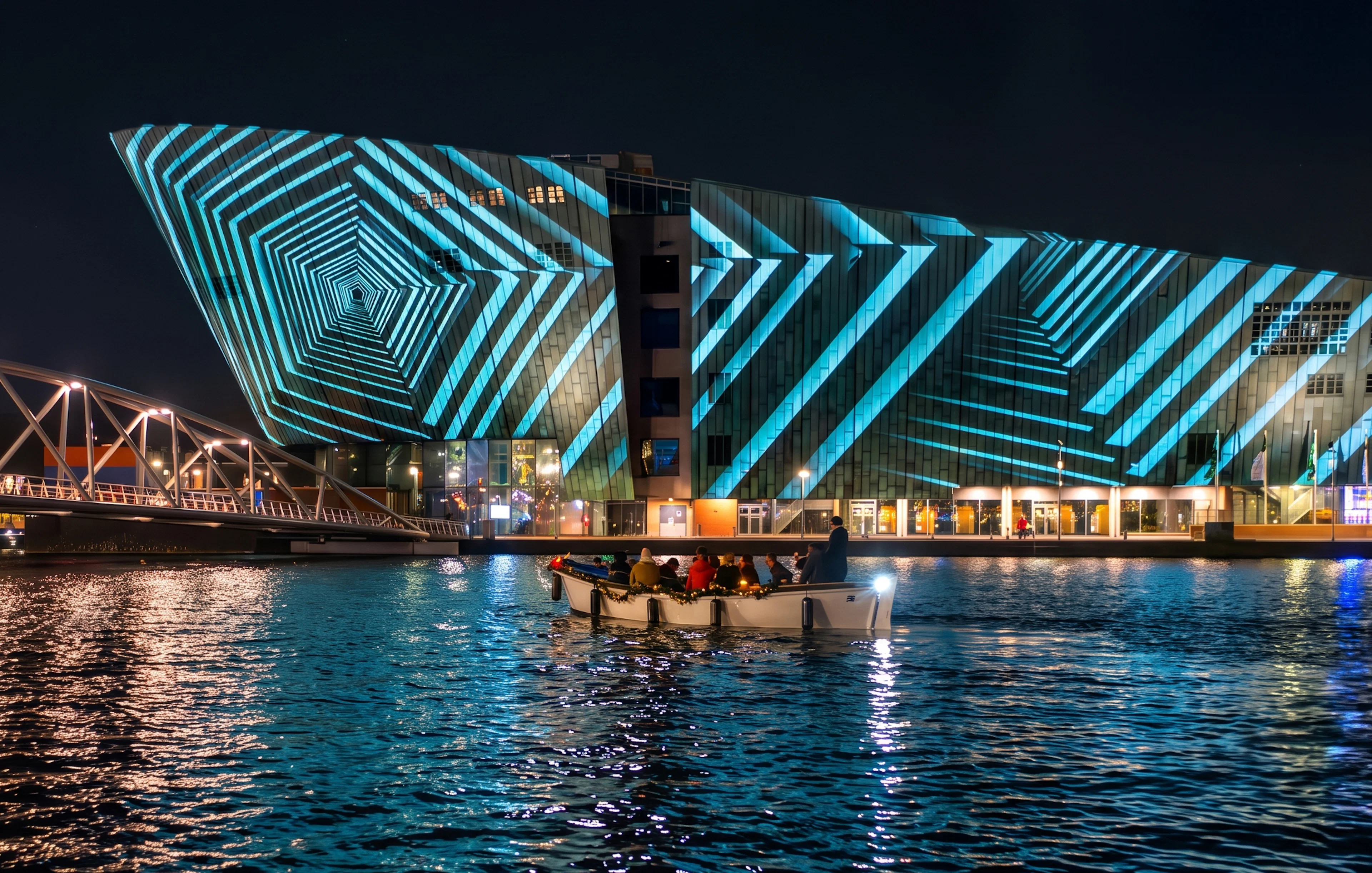 Boat tour at Amsterdam Light Festival with illuminated geometric patterns on a building.