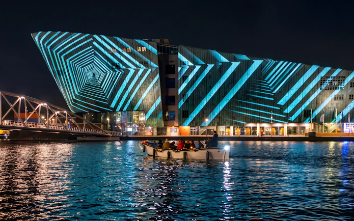 Boat tour at Amsterdam Light Festival with illuminated geometric patterns on a building.