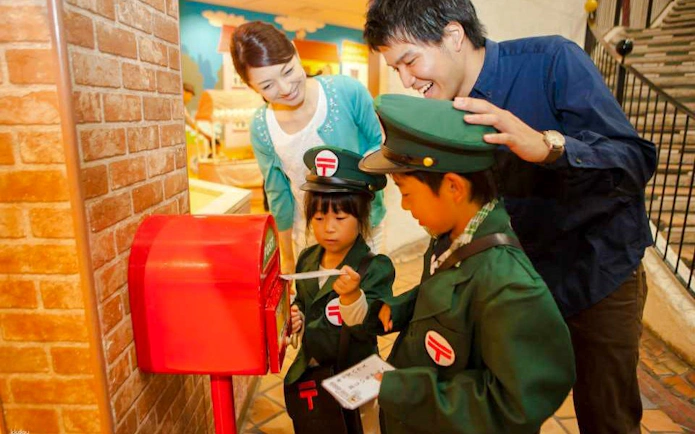 Children in uniforms interacting with a red mailbox at Kids Plaza Osaka.