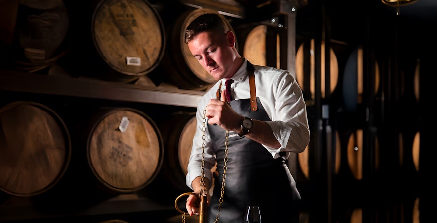 Man blending whiskey at Jameson Distillery Black Barrel class, surrounded by barrels.