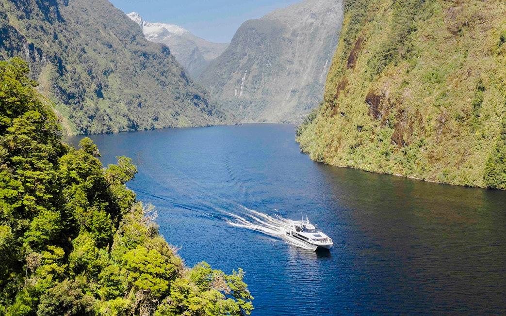 Cruise boat on Doubtful Sound with lush mountains in the background.