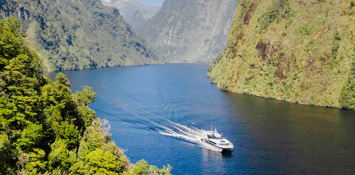 Cruise boat on Doubtful Sound with lush mountains in the background.
