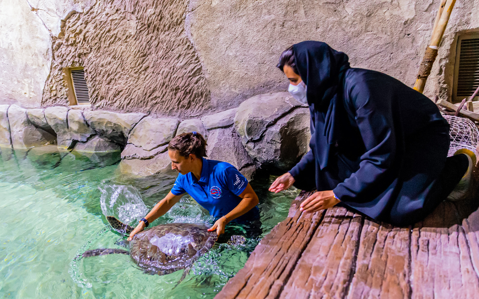 Aquarium staff member and visitor interact with a sea turtle at National Aquarium Abu Dhabi.