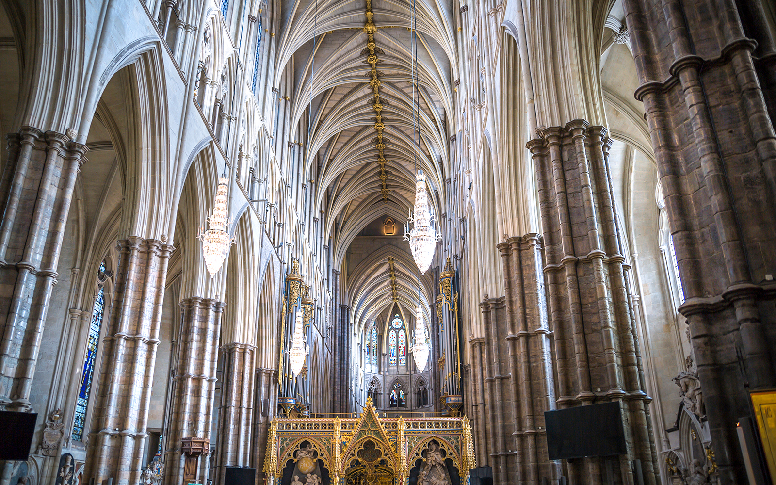 Interior view of Westminster Abbey's nave with vaulted ceilings and chandeliers.