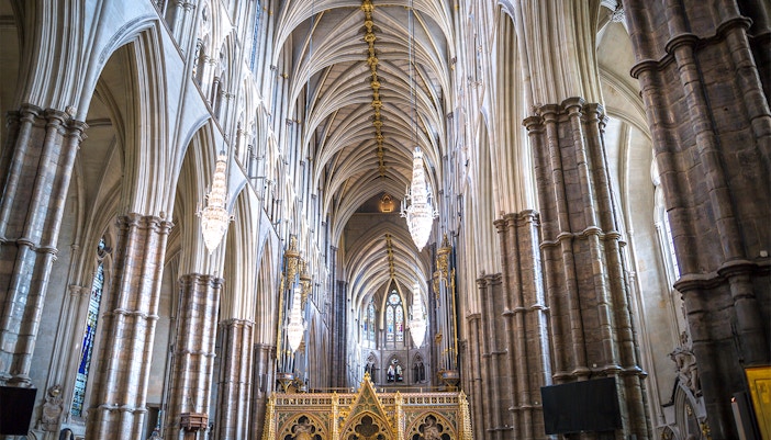 Interior view of Westminster Abbey's nave with vaulted ceilings and chandeliers.