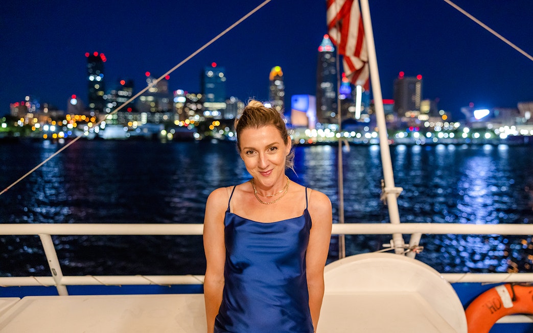 Young woman on a boat with city skyline at night in the background.