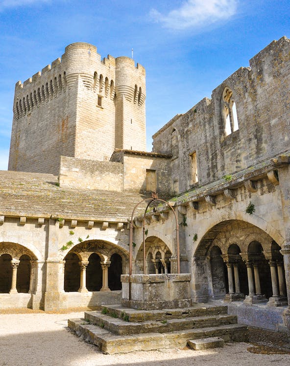 Abbey of Montmajour courtyard with stone arches and historic tower in Arles, France.