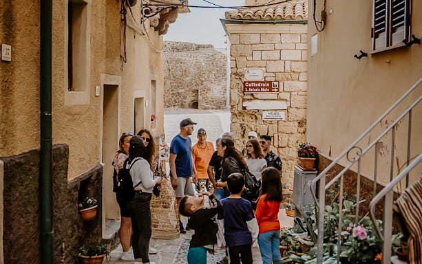 Group of tourists in a narrow street of Castelsardo during a guided tour and basket-making workshop.