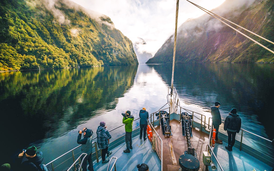 Cruise boat on Doubtful Sound with passengers photographing lush fjord scenery.