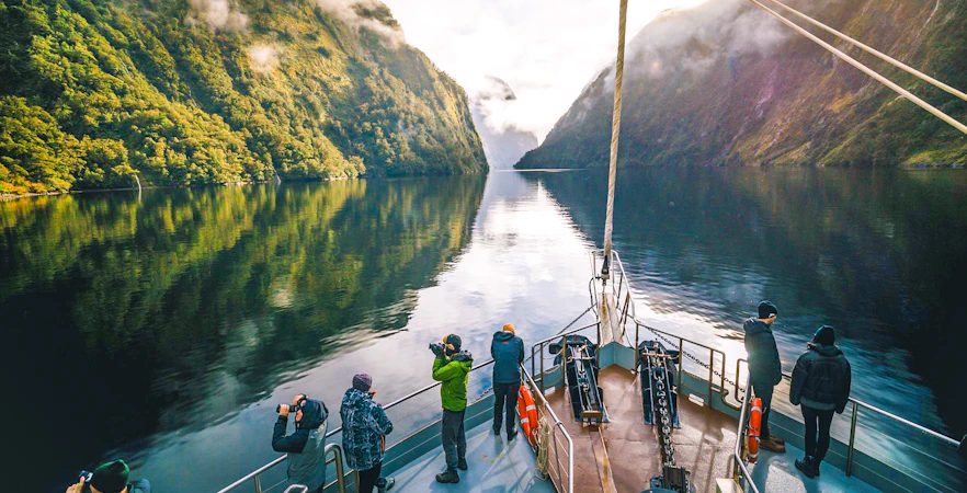 Cruise boat on Doubtful Sound with passengers photographing lush fjord scenery.