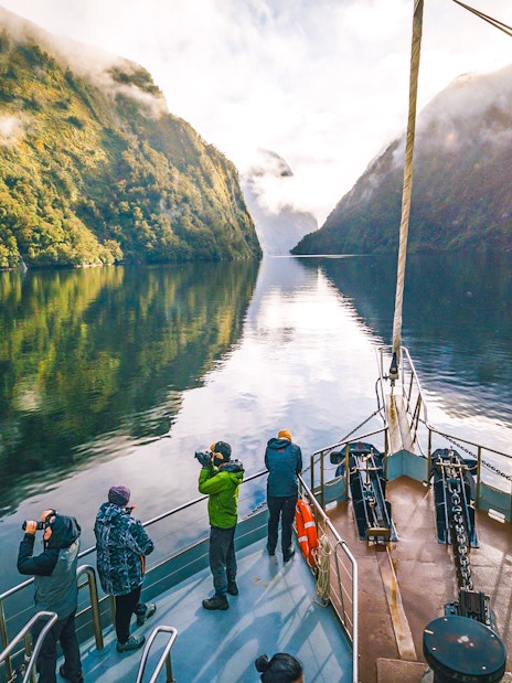 Cruise boat on Doubtful Sound with passengers photographing lush fjord scenery.