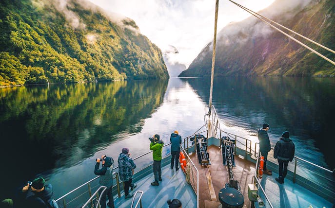Cruise boat on Doubtful Sound with passengers photographing lush fjord scenery.