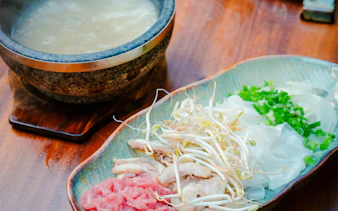 Stone bowl with pho ingredients and broth for cooking class in Hanoi.