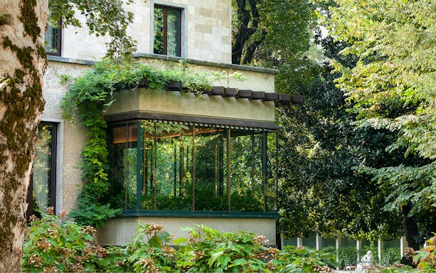 Villa Necchi Campiglio garden view with lush greenery and glass conservatory.