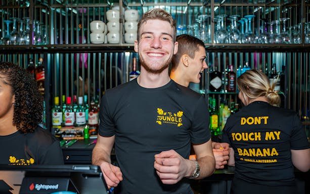 Bartenders at a lively bar in Amsterdam during a party cruise with nightclub entrance.