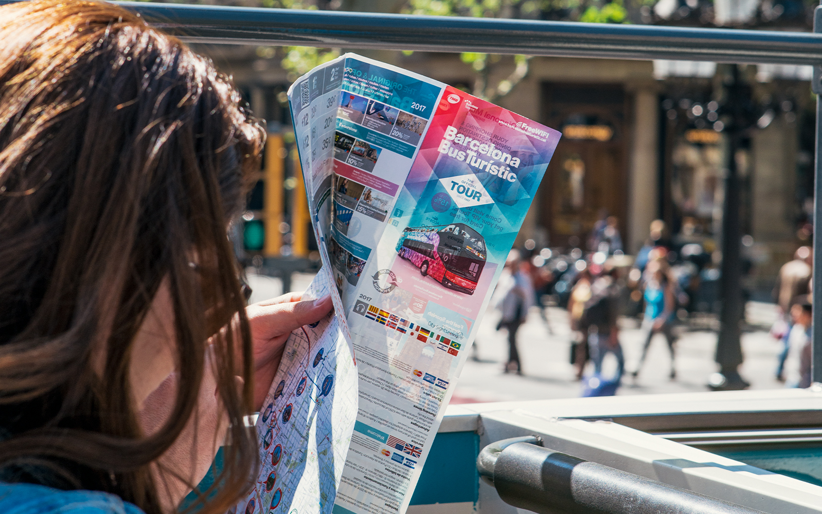 Person reading a Barcelona bus tour map on an open-top bus.