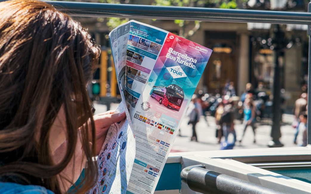 Person reading a Barcelona bus tour map on an open-top bus.